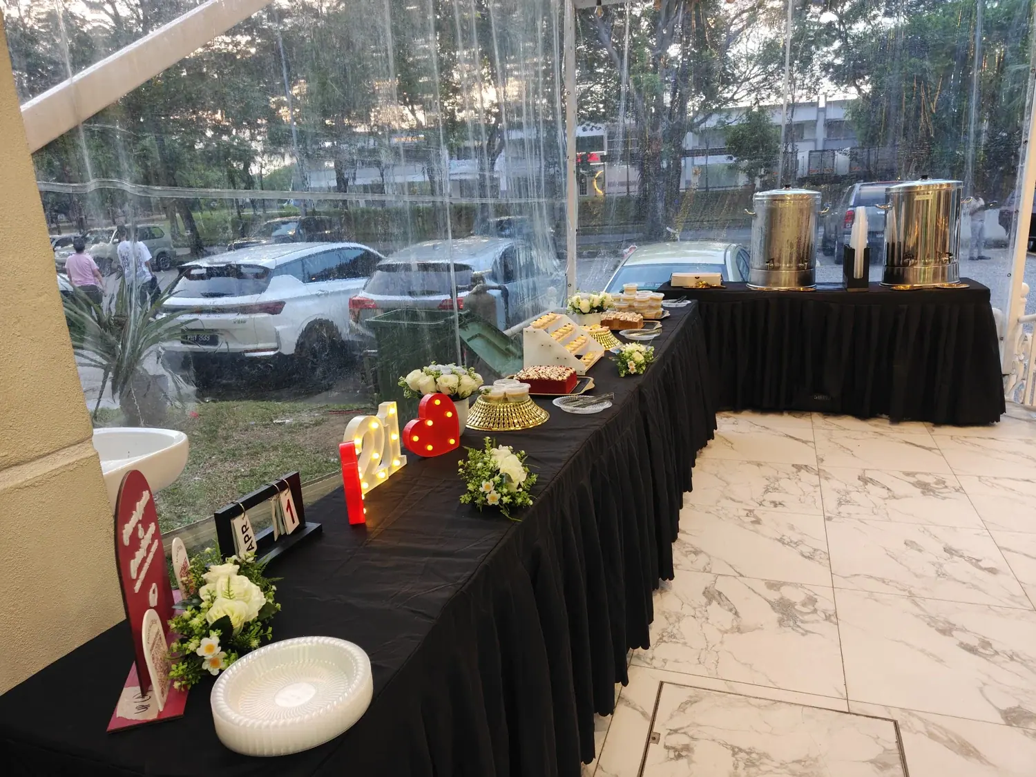 Buffet dishes arranged under cover overlooking a garden and parked cars